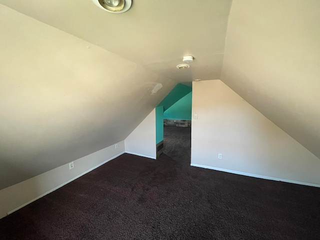 bonus room with dark colored carpet and lofted ceiling