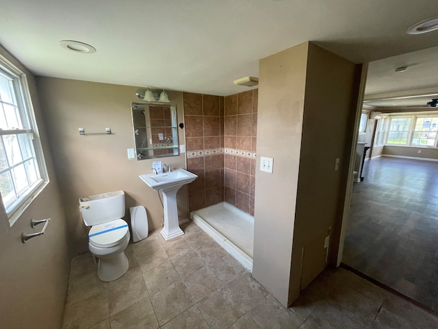 bathroom with tiled shower, toilet, and a wealth of natural light