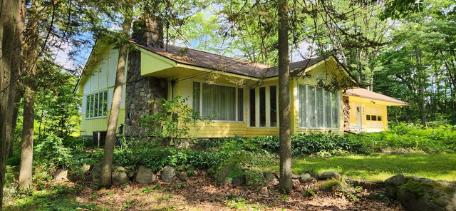 227 Joliet Ave, Houghton Lake, MI 48629 - view of home's exterior featuring a chimney, stone siding, and board and batten siding