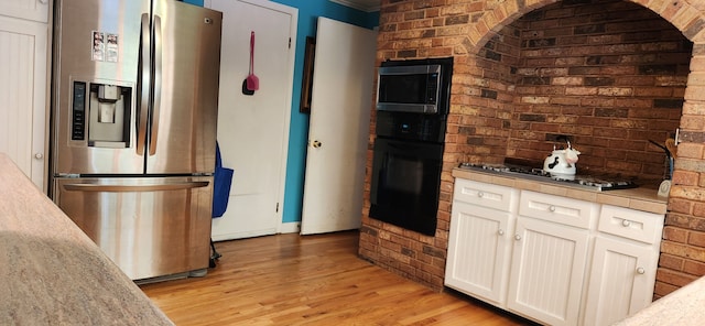 kitchen featuring white cabinets, appliances with stainless steel finishes, light hardwood / wood-style flooring, and brick wall