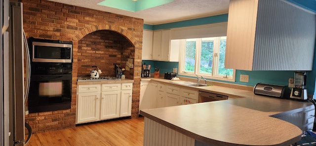 kitchen featuring kitchen peninsula, appliances with stainless steel finishes, light wood-type flooring, brick wall, and sink