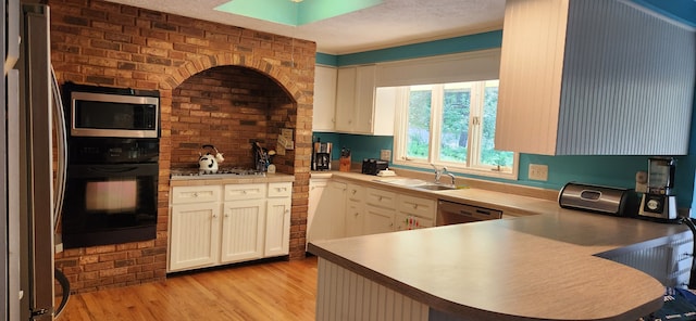 227 Joliet Ave, Houghton Lake, MI 48629 - kitchen with stainless steel appliances, a sink, light wood-style floors, a peninsula, and white cabinetry