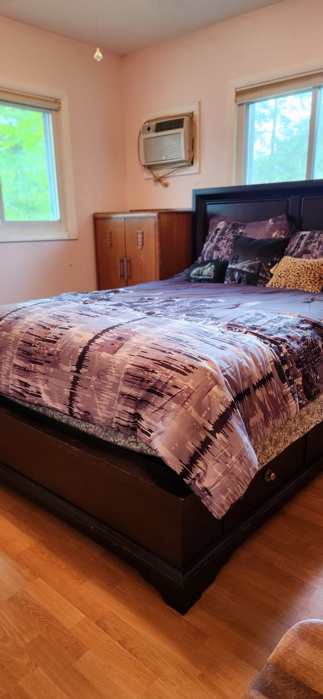 bedroom with multiple windows, a wall unit AC, and light hardwood / wood-style flooring