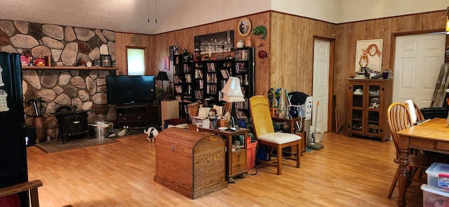 living room with wood walls, light hardwood / wood-style floors, a wood stove, and high vaulted ceiling