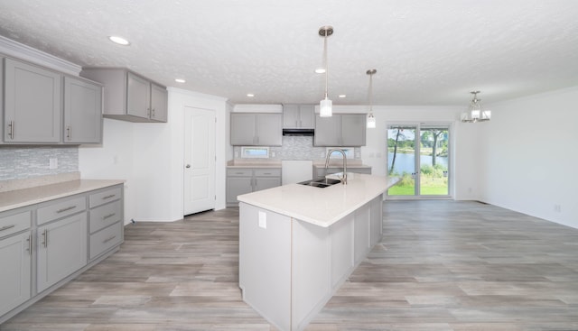 kitchen featuring gray cabinets, a kitchen island with sink, sink, and decorative light fixtures