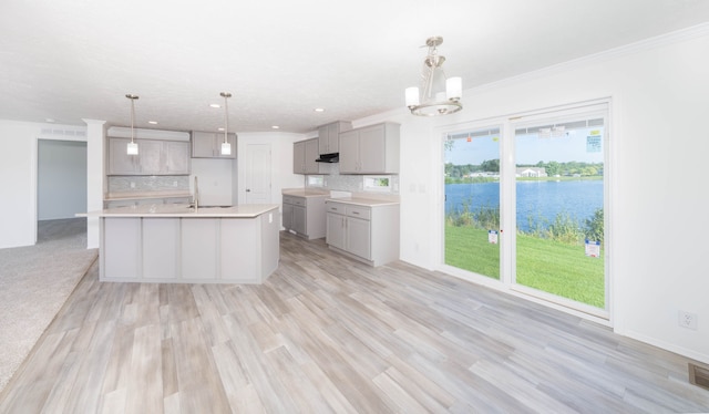 kitchen with light wood-type flooring, a center island with sink, a water view, gray cabinets, and hanging light fixtures