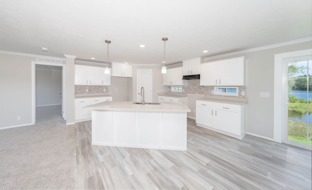 kitchen with sink, pendant lighting, light hardwood / wood-style flooring, white cabinetry, and an island with sink