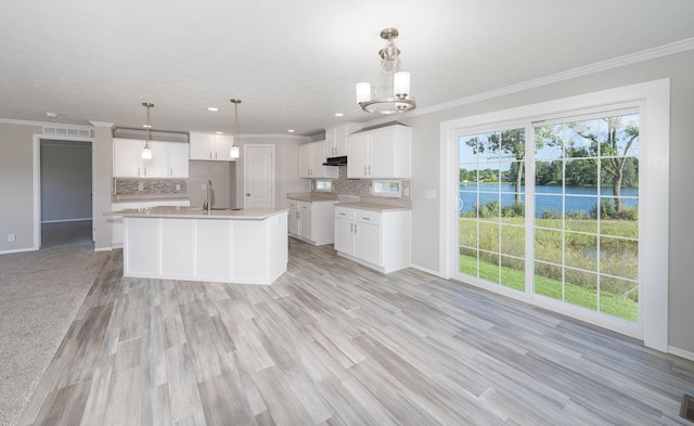 kitchen featuring sink, pendant lighting, a water view, white cabinets, and an island with sink