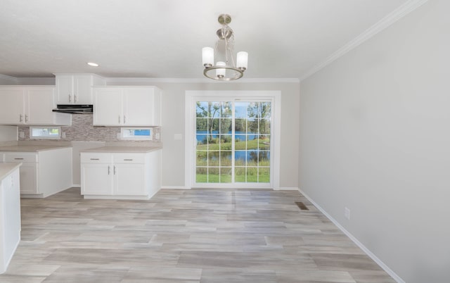 kitchen featuring pendant lighting, white cabinetry, crown molding, and a chandelier