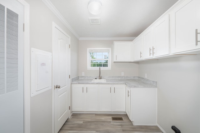 kitchen featuring a textured ceiling, crown molding, sink, light hardwood / wood-style flooring, and white cabinetry