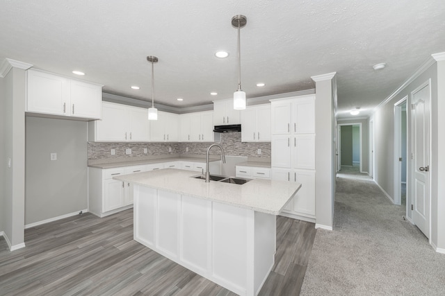 kitchen with a center island with sink, white cabinets, sink, light hardwood / wood-style flooring, and decorative light fixtures