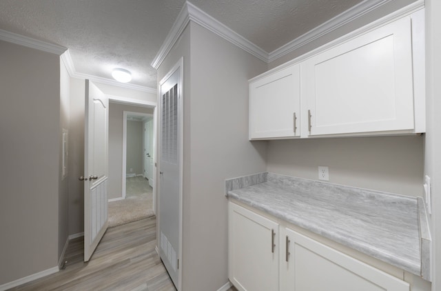 laundry area featuring a textured ceiling, light hardwood / wood-style floors, and crown molding