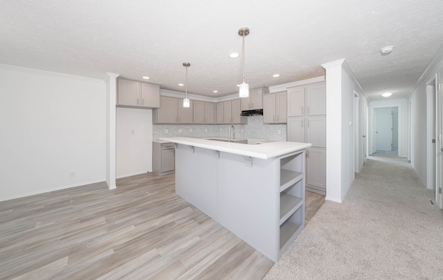 kitchen featuring gray cabinetry, pendant lighting, a kitchen island with sink, crown molding, and light wood-type flooring