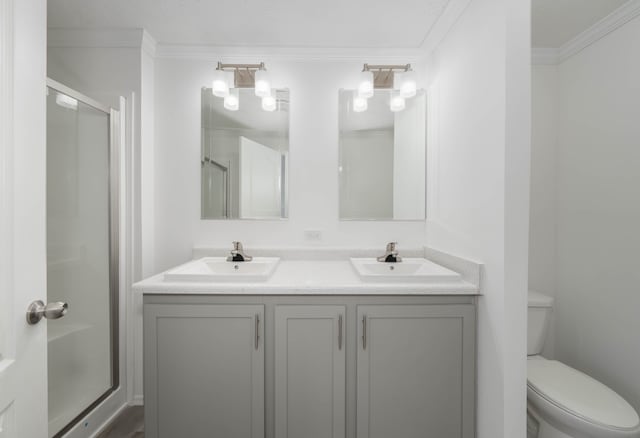 bathroom featuring vanity, toilet, a shower with door, and ornamental molding