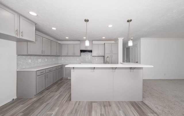 kitchen featuring gray cabinetry, hanging light fixtures, light hardwood / wood-style flooring, backsplash, and a kitchen island with sink