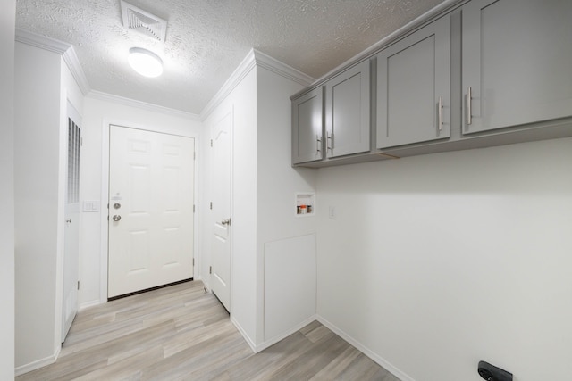 clothes washing area featuring cabinets, crown molding, hookup for a washing machine, a textured ceiling, and light wood-type flooring