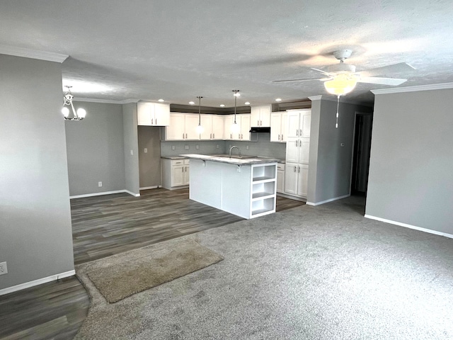 kitchen featuring white cabinets, crown molding, hanging light fixtures, dark hardwood / wood-style floors, and an island with sink