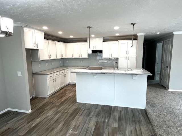 kitchen with pendant lighting, white cabinets, a center island with sink, crown molding, and dark hardwood / wood-style flooring