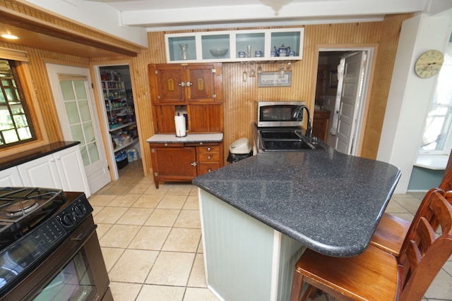 kitchen with a kitchen bar, black stove, sink, light tile patterned floors, and beam ceiling