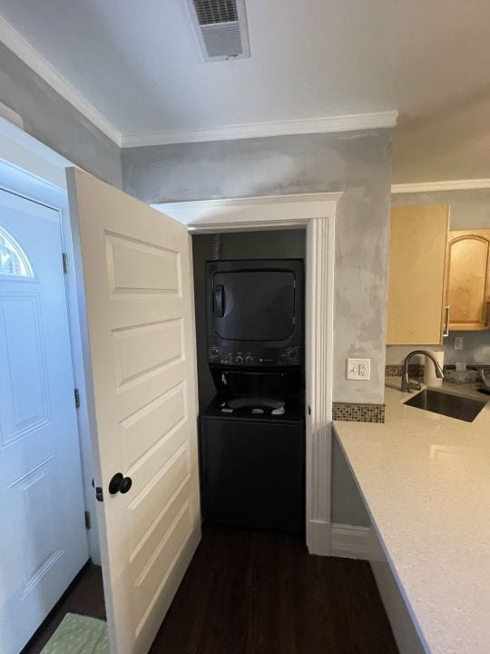 hallway featuring stacked washer / dryer, sink, dark wood-type flooring, and ornamental molding