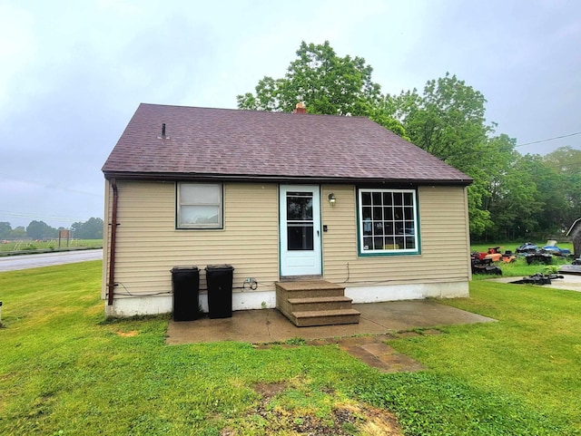 rear view of house featuring entry steps, roof with shingles, and a yard