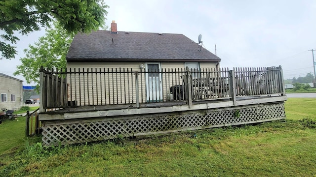 back of house with a deck, a lawn, and roof with shingles