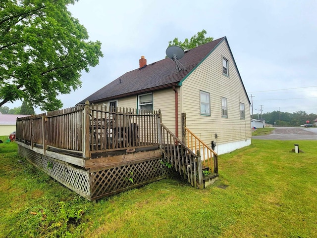 back of house featuring a chimney, a deck, a lawn, and roof with shingles