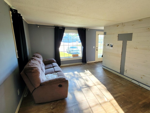 living area featuring a textured ceiling, hardwood / wood-style floors, wood walls, and baseboards