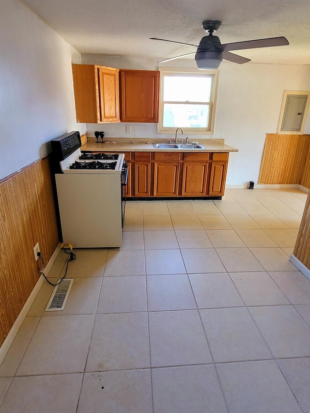 kitchen with wooden walls, visible vents, brown cabinetry, range with gas cooktop, and a sink