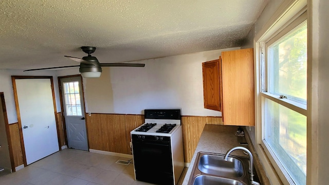 kitchen with range with gas stovetop, brown cabinets, wainscoting, a sink, and wood walls