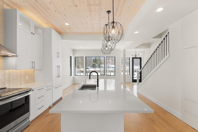 kitchen featuring a center island with sink, stainless steel electric range oven, sink, white cabinetry, and an inviting chandelier