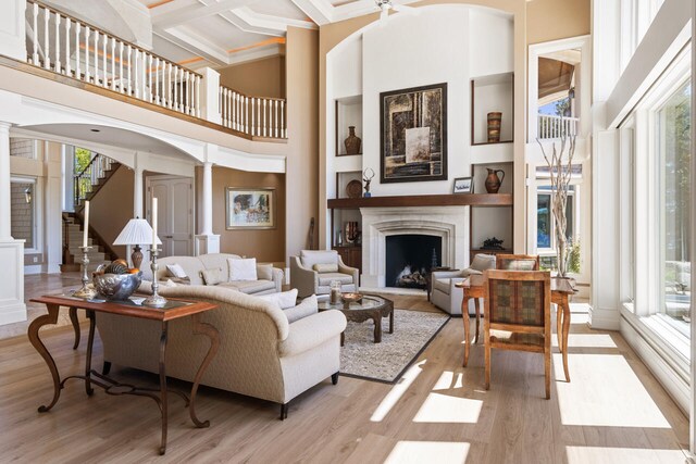7545 Oyster Bay Dr Unit 4, Charlevoix, MI 49720 - living room featuring ornate columns, a towering ceiling, a fireplace with raised hearth, light wood finished floors, and coffered ceiling