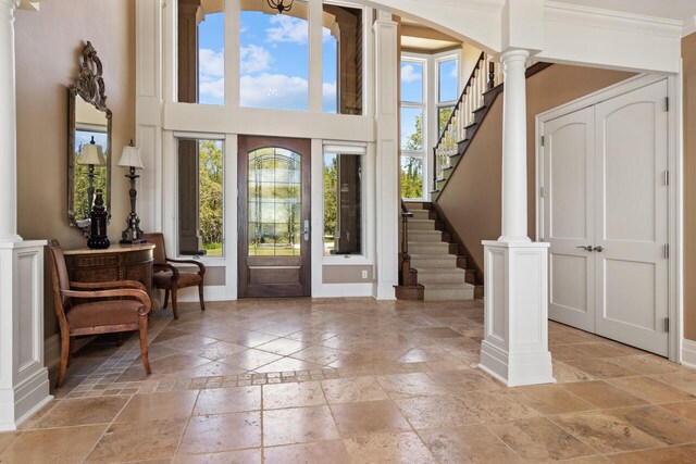 7545 Oyster Bay Dr Unit 4, Charlevoix, MI 49720 - foyer featuring stone tile floors, ornate columns, baseboards, a high ceiling, and stairway