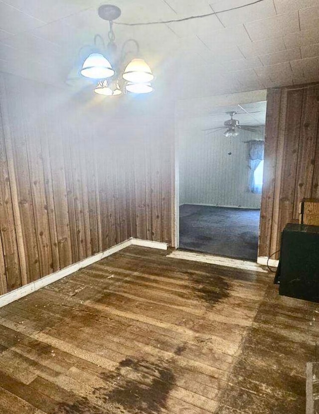 empty room with ceiling fan with notable chandelier, dark wood-type flooring, and wood walls