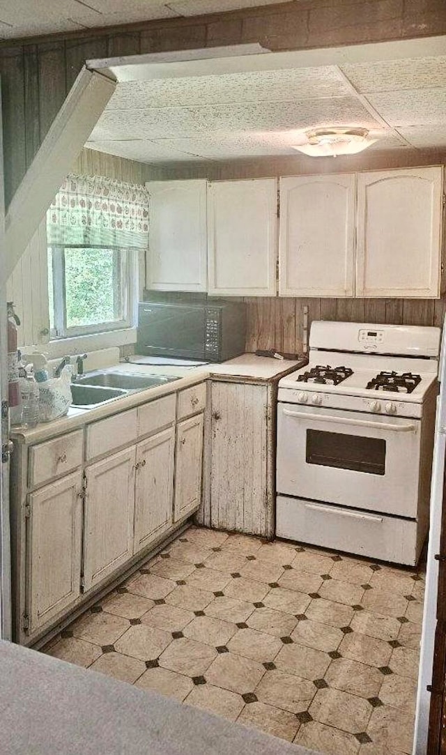 kitchen featuring white range with gas stovetop, sink, and wooden walls