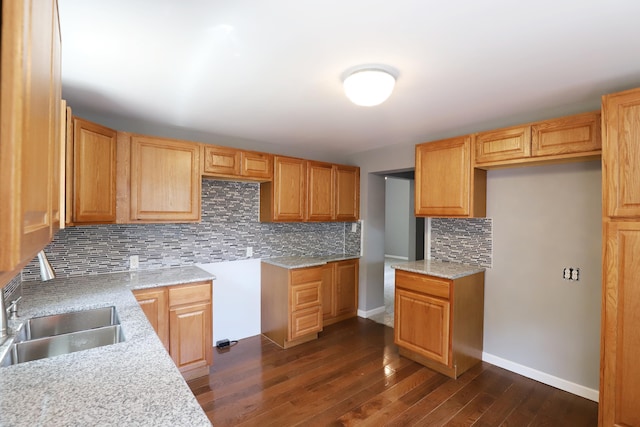 kitchen with tasteful backsplash, light stone counters, dark hardwood / wood-style floors, and sink