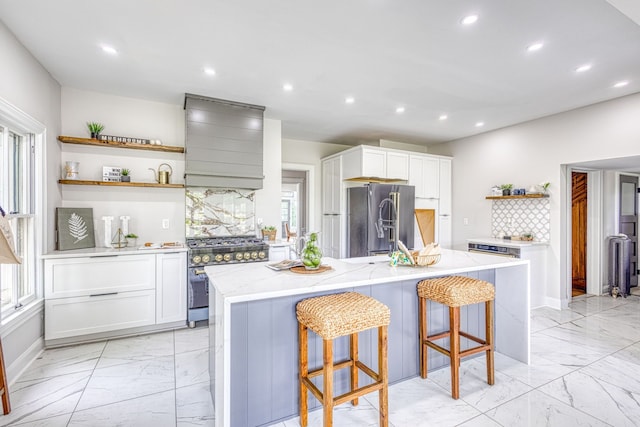 kitchen featuring high end appliances, white cabinets, an island with sink, a kitchen bar, and custom range hood