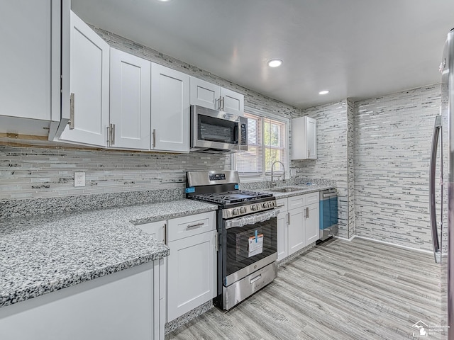 kitchen featuring white cabinetry, sink, light stone counters, appliances with stainless steel finishes, and light wood-type flooring