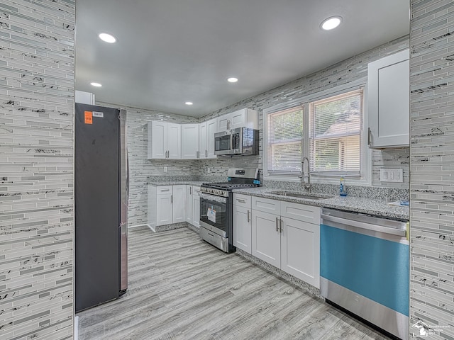 kitchen with light stone countertops, sink, light hardwood / wood-style flooring, white cabinets, and appliances with stainless steel finishes