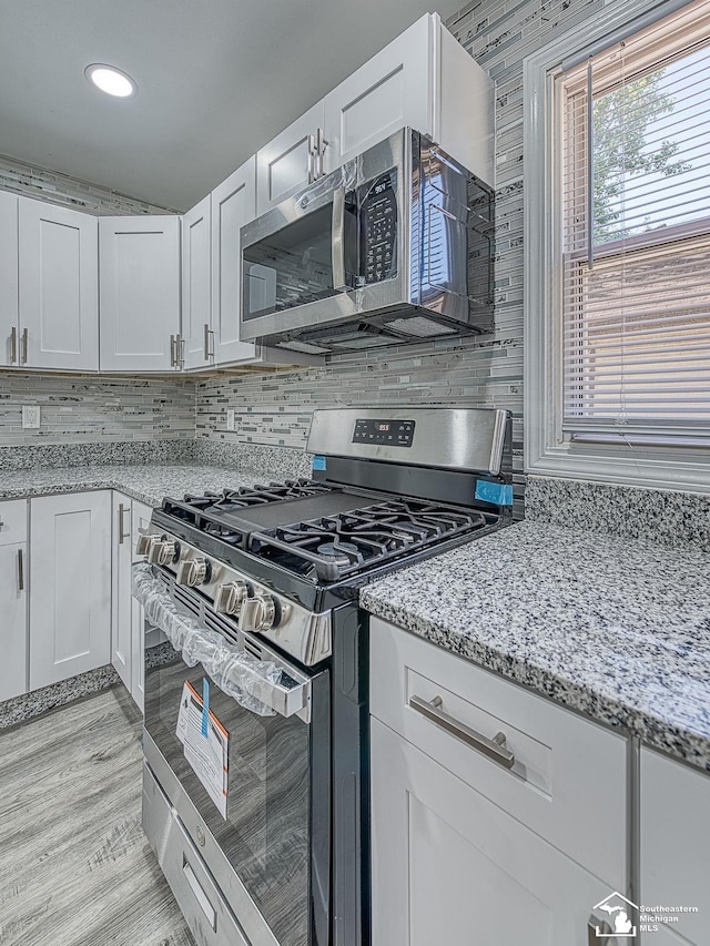 kitchen featuring decorative backsplash, white cabinetry, light stone counters, and appliances with stainless steel finishes