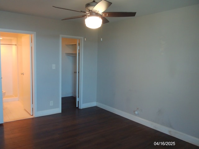 unfurnished bedroom with a spacious closet, baseboards, a closet, and dark wood finished floors