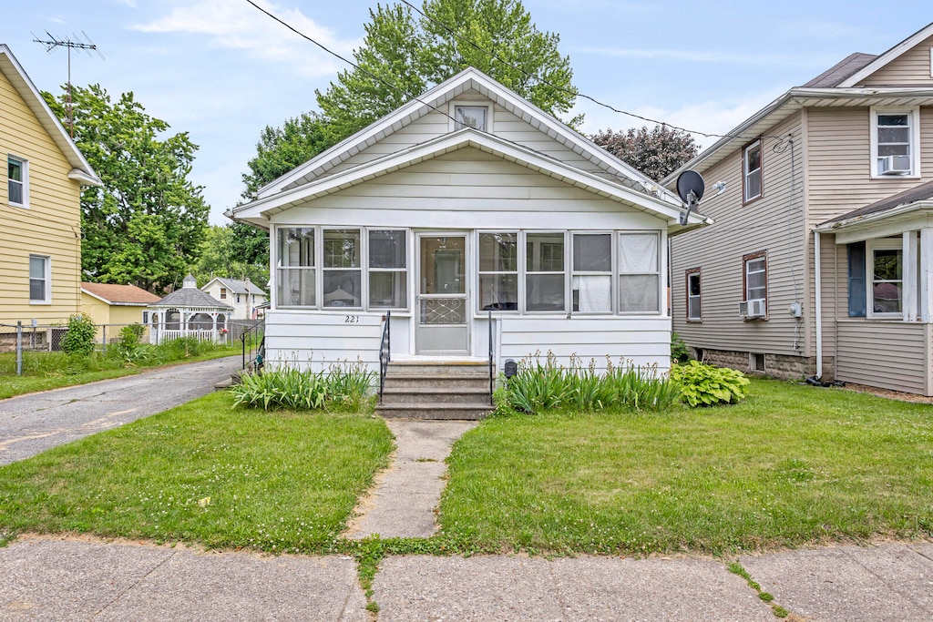 bungalow featuring cooling unit, a sunroom, and a front lawn