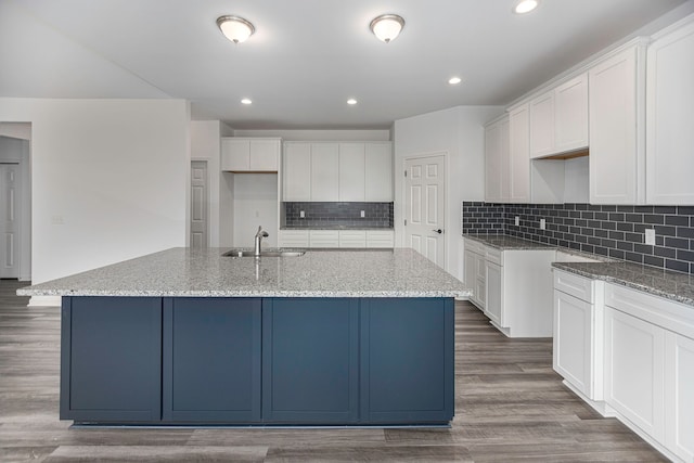 kitchen with white cabinets, dark hardwood / wood-style flooring, light stone counters, and a kitchen island with sink