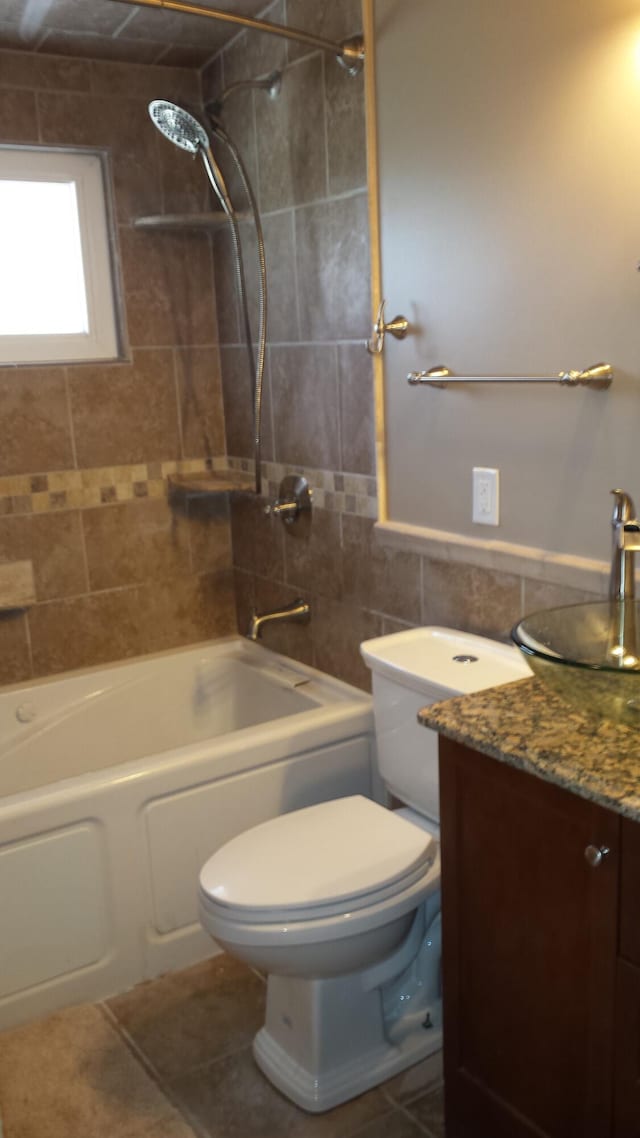 full bathroom with tiled shower / bath combo, tile patterned flooring, toilet, vanity, and tile walls