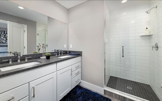 full bath featuring a sink, a shower stall, baseboards, and double vanity