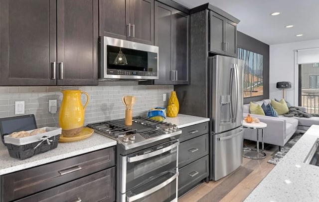 kitchen featuring light hardwood / wood-style flooring, decorative backsplash, light stone countertops, appliances with stainless steel finishes, and dark brown cabinetry