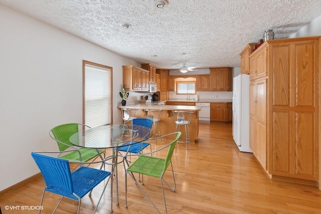 kitchen featuring a kitchen bar, kitchen peninsula, white appliances, and light wood-type flooring