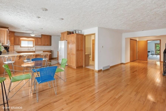 kitchen with kitchen peninsula, a breakfast bar, a textured ceiling, white refrigerator, and light hardwood / wood-style floors