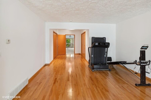exercise room with a textured ceiling and light hardwood / wood-style flooring