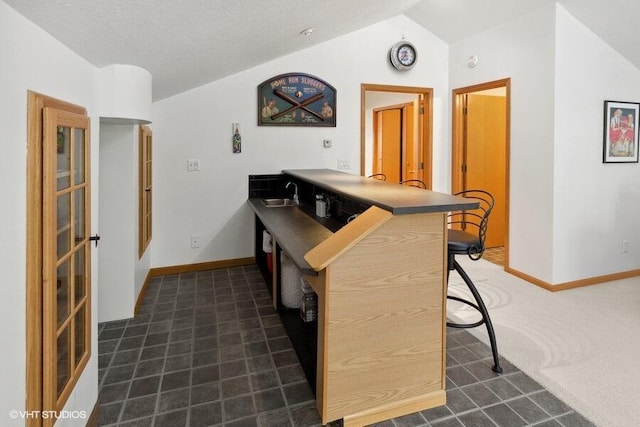kitchen with sink, a kitchen breakfast bar, kitchen peninsula, lofted ceiling, and dark carpet